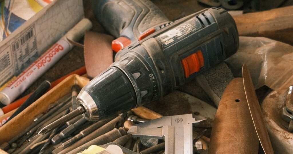 A worn cordless drill among assorted hand tools on a cluttered workbench